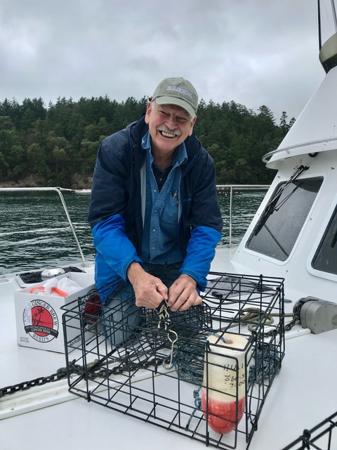 Stephen Hulley, pictured on a boat in the Puget Sound, smiling while holding a crab trap